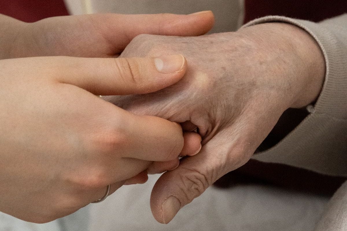 Deux mains jeunes tenant doucement la main d'une personne âgée assise dans un fauteuil