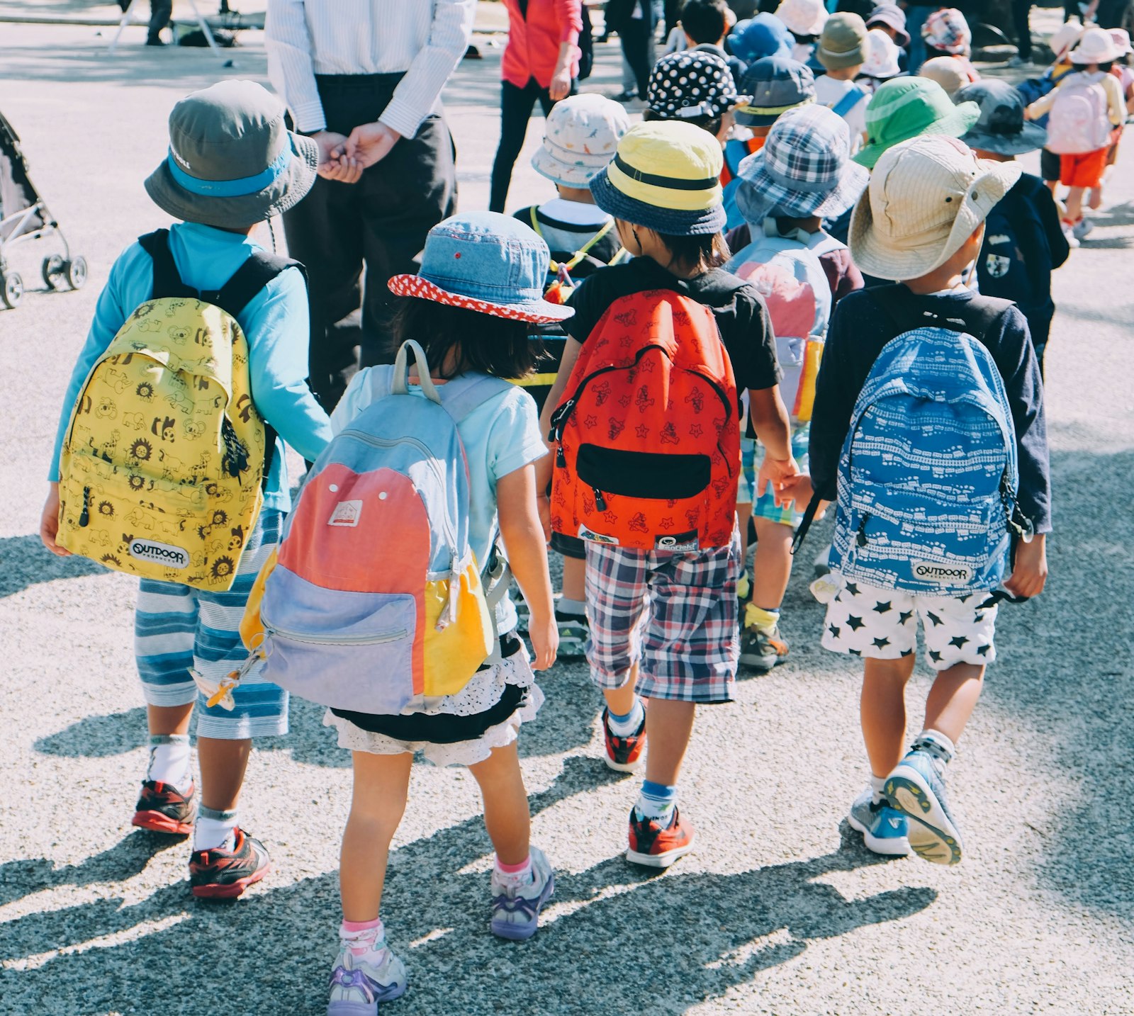 Groupe d'enfants avec cartables marchant vers l'école, vus de dos
