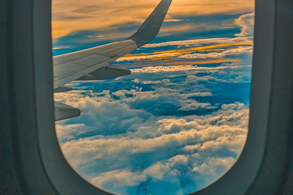 Vue de hublot d'avion au coucher du soleil, aile et mer de nuages