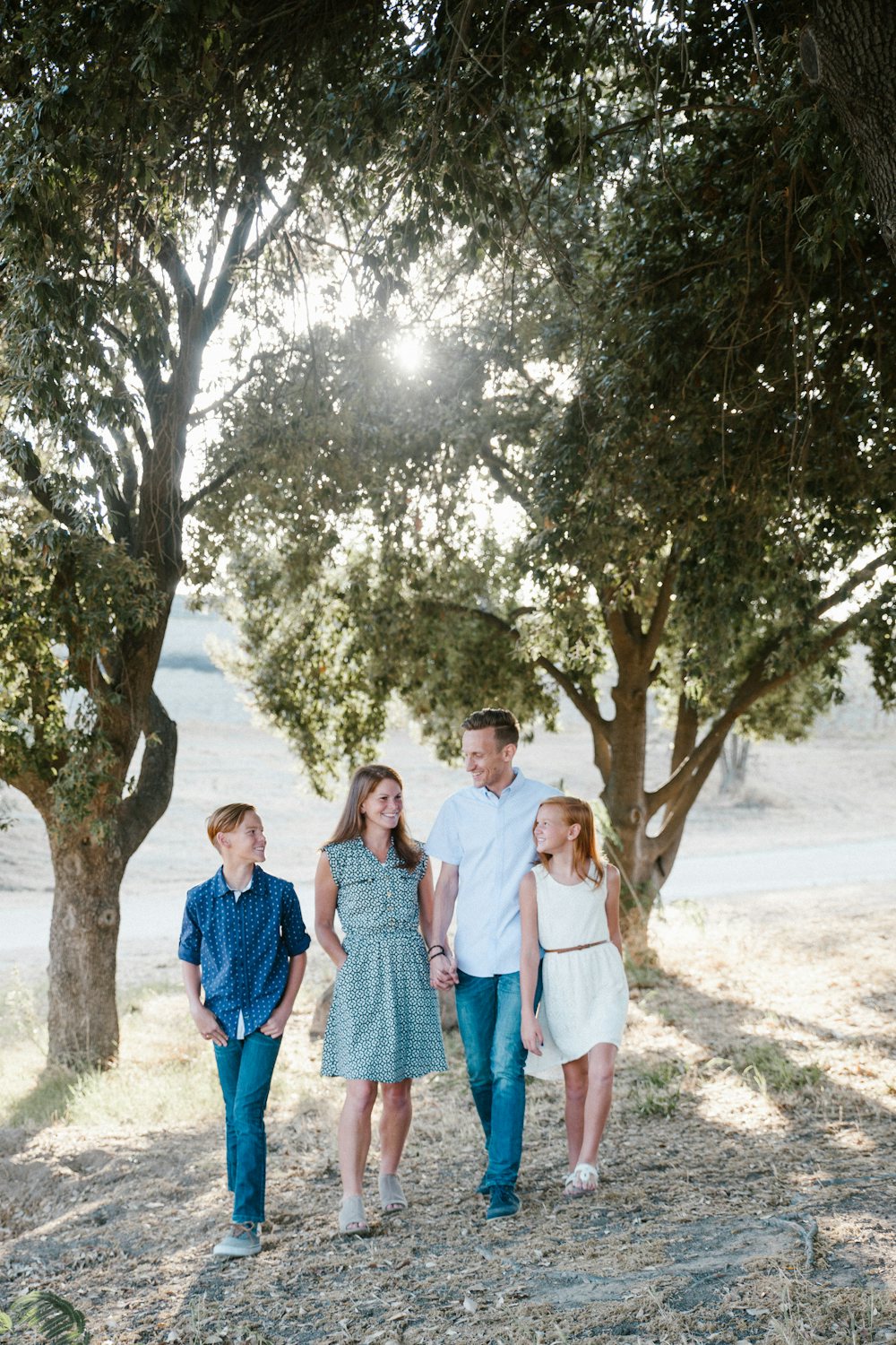 Une famille avec deux enfants pré-adolescents marchant ensemble sous les arbres, complices